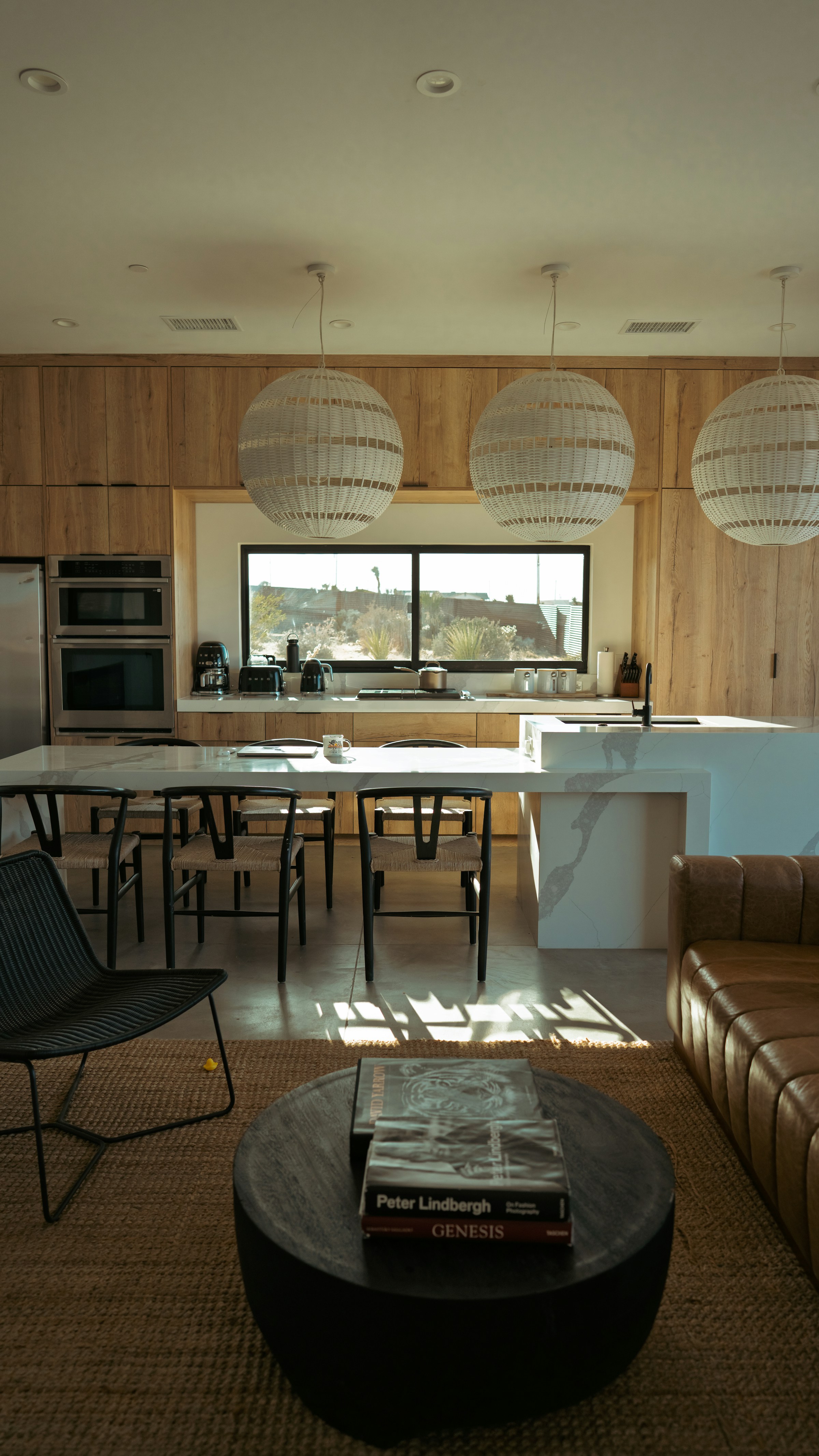 Sunlit kitchen with oak cabinetry, a white stone island, and woven pendant lights